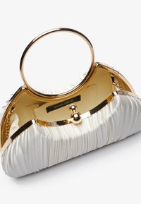 Sac à main plissé blanc avec une poignée ronde en métal doré, présentant une texture douce, un matériel doré et une étiquette intérieure beige.