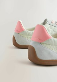 Paire de baskets gris clair et blanches avec des accents roses au talon et des semelles marron, vues de dos sur un fond uni.