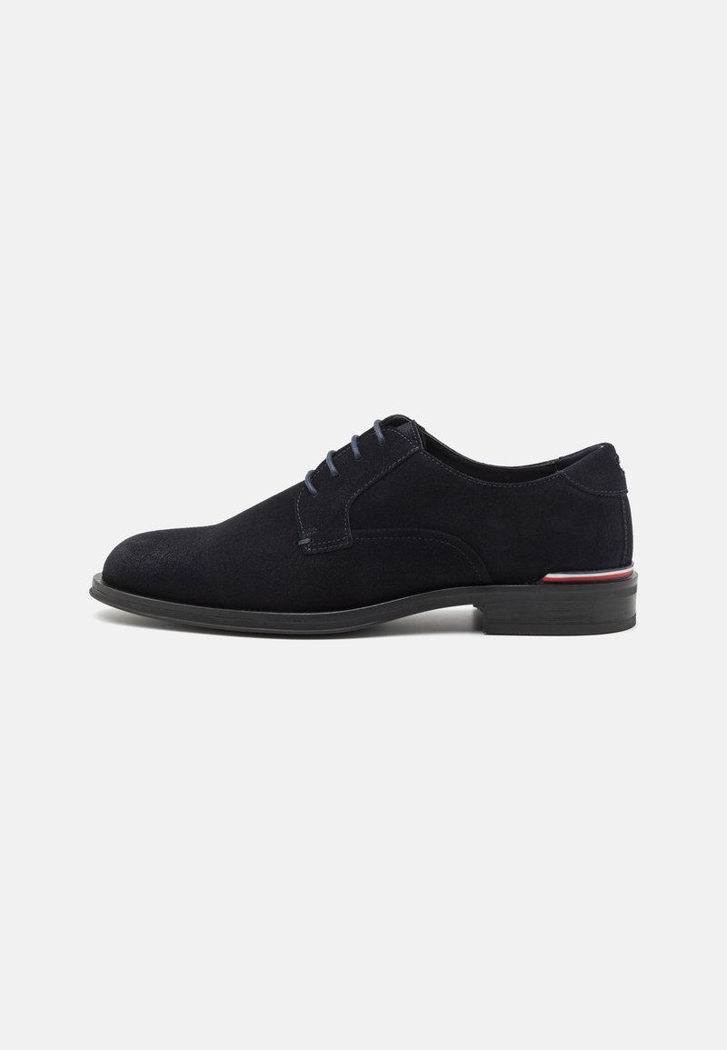 Chaussure habillée pour homme en suède noir avec fermeture à lacets et talon bas, comportant un détail de fine bande rouge et blanche sur la semelle.