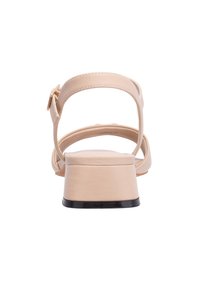 Sandali con tacco beige dal finish liscio, con cinturino alla caviglia e tacco a blocco basso con un accento nero. Design aperto sul retro con dettagli intagliati.