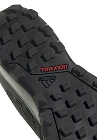Czarna gumowa podeszwa z głębokim bieżnikiem dla lepszej przyczepności, z napisem "TRAXION" w kolorze czerwonym. Zawiera teksturowany bok oraz logo Adidasa na pięcie.