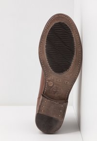 Suola di scarpa in pelle marrone che mostra la taglia 37, bordi cuciti, texture nelle aree del tallone e della pianta, posizionata in angolo su uno sfondo bianco.