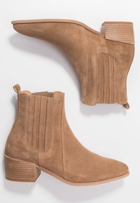 Bottines en suede beige avec un bout pointu, des panneaux latéraux à côtes et un talon empilé. Texture lisse, dotées d'une languette pour un enfilage facile.