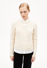 Crème ribgebreide trui met een ronde hals en textuurpatroon, gelaagd over een witte overhemd met kraag, met aansluitende lange mouwen.