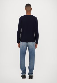 Pulover tricotat de culoare bleu marin, cu mâneci lungi, purtat cu blugi din denim de culoare bleu deschis. Puloverul are un guler și manșete cu dantelă, iar blugii au buzunare la spate.