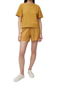 Camiseta de algodón amarilla mostaza con mangas cortas y un diseño cropped, combinada con pantalones cortos a juego que cuentan con una cinturilla elástica y cordón.