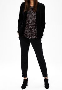 Blazer di velluto nero sopra una blusa a pois, abbinato a pantaloni neri a sigaretta e stivaletti neri. I punti chiave includono texture e motivo.
