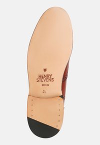 Leder-Schuhsohle in hellbrauner Farbe mit schwarzen Akzenten an der Ferse und dem eingestempelten Markenlabel "HENRY STEVENS BERLIN" in dunkelbraun.