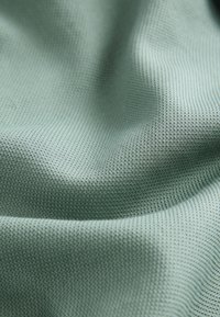 Tissu vert pâle texturé avec un petit motif gaufré créant de doux plis et des ombres.