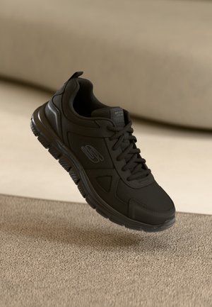 Black athletic shoe made of mesh and synthetic material. Features thick sole, rounded toe, and lace-up design with side branding detail.