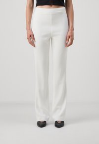 Pantaloni bianchi su misura con una texture liscia e un design a gamba dritta. Presentano una vita media e sono abbinati a scarpe nere.
