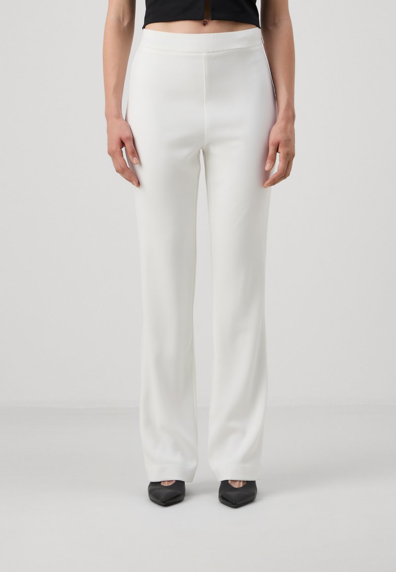 Pantaloni bianchi su misura con una texture liscia e un design a gamba dritta. Presentano una vita media e sono abbinati a scarpe nere.