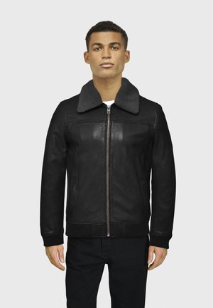 Chaqueta de cuero negra con un suave collar gris, cremallera frontal, puños acanalados y dobladillo. Textura suave y diseño ajustado, estilizada para mantener el calor.