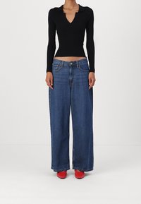 Černý žebrovaný top s dlouhým rukávem a výstřihem do V, doplněný širokými modrými džíny a červenými botami na blokovém podpatku.