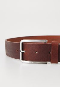 Ceinture en cuir marron avec une finition texturée, dotée d'une boucle rectangulaire en métal argenté et de plusieurs trous d'ajustement. Nom de la marque gravé sur la boucle.