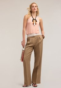 Top fără mâneci, de culoare roz deschis, cu un tiv stratificat, asortat cu pantaloni bej cu talie înaltă. Accesorizat cu un colier cu ciucuri multicolori și o geantă.