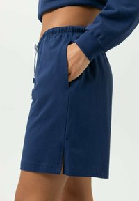 Shorts en coton bleu marine avec une taille élastique, un cordon blanc, des poches latérales et de petites fentes sur les côtés pour faciliter les mouvements.