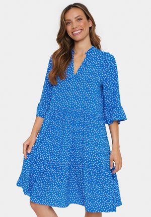 Rochie albastră cu guler și mâneci trei sferturi, cu un model floral. Designul include o fustă stratificată pentru un plus de volum.