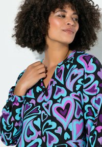 Langarmbluse aus schwarzem Stoff mit einem Muster aus bunten Herzen in Pink, Lila und Blau. V-Ausschnitt und geraffte Ärmel.