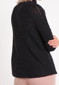 Maglione nero lavorato a maglia con collo alto, tessuto a trama, fessure laterali e dettagli con bottoni lungo l'orlo. Vestibilità rilassata con polsini a costine.