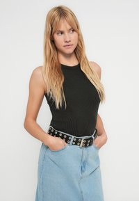 Black ribbed tank top with a high neckline, paired with a light denim skirt and a black belt featuring metal grommets.