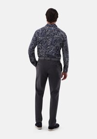 Männershirt mit dunklem Muster und Paisleymuster, kombiniert mit grauen Hosen und marineblauen Schuhen, von hinten betrachtet.