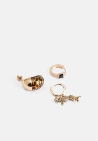 Guldfärgad smyckeset: ett örhänge med leopardmönster, en pinky-ring med en svart sten, och en guldfärgad djurformad berlock på ett hoop-örhänge.