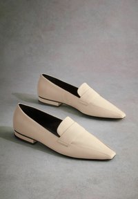 Mocassins en cuir beige avec un orteil pointu et une sangle cousue sur le dessus, dotés d'un petit talon rectangulaire et d'une texture lisse.