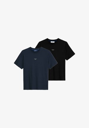 Mann trägt schwarzes Marc O’Polo Denim T-Shirt, leicht in hellblaue Jeans gesteckt, Hände in den Taschen, am Hals und an den Oberschenkeln beschnitten.