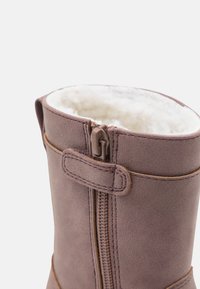 Brun kunstlæderstøvle med en struktureret overflade, med en sidelukning og en fluffy hvid foret øverst for ekstra komfort.