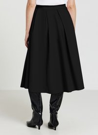 Gonna nera a trapezio con pieghe sul retro, realizzata in un materiale morbido, abbinata a stivali neri al ginocchio e una maglietta bianca semplice.