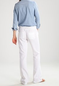 Pantalons évasés blancs avec une taille élastique et deux poches arrière, associés à une chemise à manches longues bleu clair. Texture de tissu lisse.