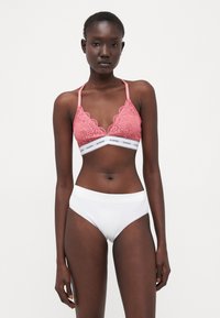 Bralette in pizzo rosa con spalline regolabili e una fascia elastica bianca con il nome del marchio; abbinato a culotte bianche a vita alta.