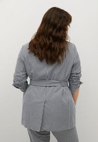 Czarnobiały żakiet w kratę gingham z paskiem w talii, podwiniętymi rękawami i wentylacją z tyłu, w zestawie z pasującymi spodniami w ten sam wzór.