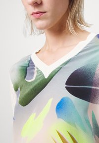 V-Ausschnitt-Oberteil mit einem bunten, abstrakten Design in grünen, blauen und gelben Farben auf einem hellen Hintergrund. Weicher, leichter Stoff.