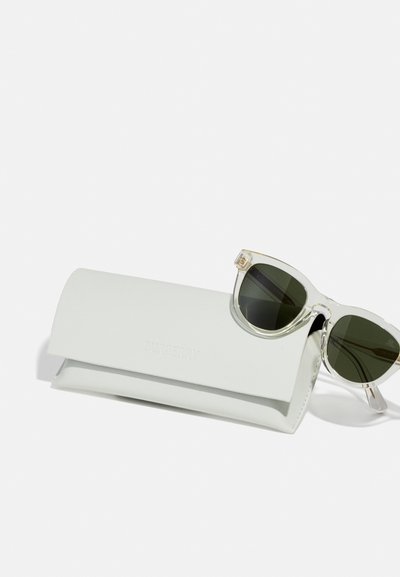Óculos de sol Burberry com lentes verdes, armações de plástico transparente e acentos prateados, posicionados ao lado de um estojo de couro branco com logótipo em relevo.