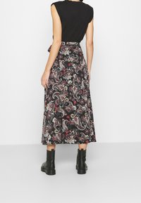 Jupe longue noire avec un motif paisley intriqué en rouge, crème et or. Le matériau semble doux, avec un design fluide et un détail de taille nouée.
