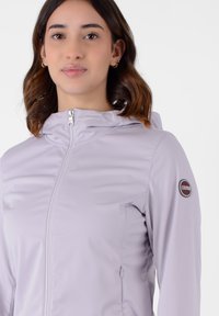 Giacca zip-up di un leggero lavanda con cappuccio, dotata di una toppa con logo sulla manica, realizzata in tessuto liscio e elastico.