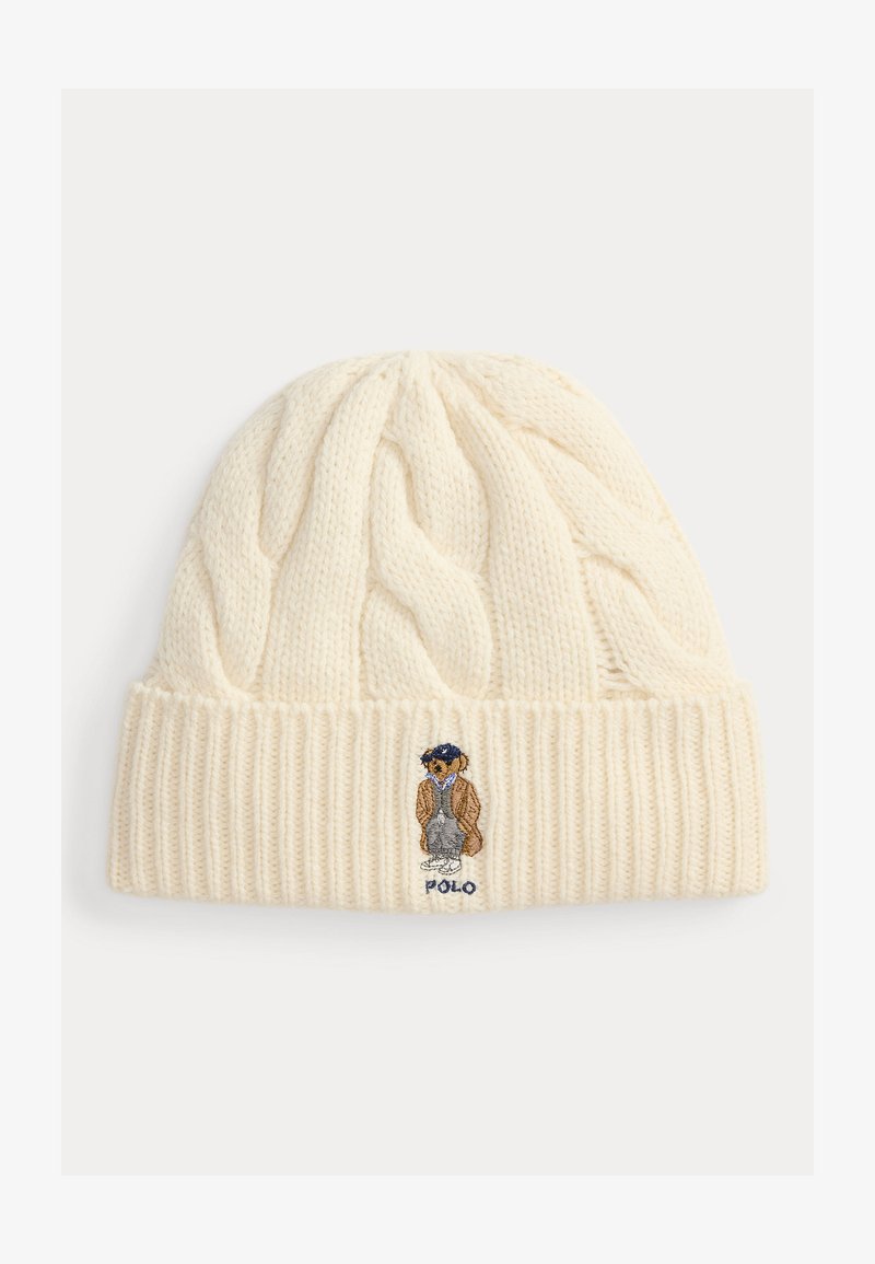 Bílá pletená čepice s copánkovým vzorem a žebrovaným lemem. Vyšitý motiv medvěda v oblečení s textem "POLO" pod ním.