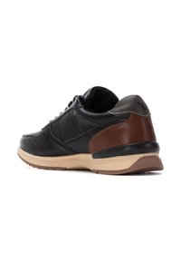 Zapatilla negra de cuero con acentos marrones, suela de goma, cuello acolchado y detalles de costura. Cuenta con cierre de cordones y texturas contrastantes.