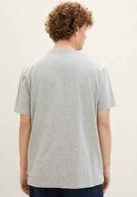 Camiseta de algodón gris con mangas cortas, que presenta un cuello redondo y un sutil detalle de logo cerca del dobladillo. Textura suave, ajuste regular.
