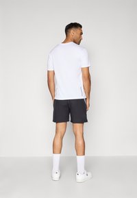 Camisa blanca de manga corta, pantalones cortos negros, calcetines blancos y zapatillas blancas. La camisa tiene un cuello redondo y está hecha de una tela suave.