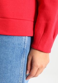 Rode top met lange mouwen van zachte stof, met een aansluitende tailleband en geribde manchetten, gecombineerd met lichtblauwe denim jeans.