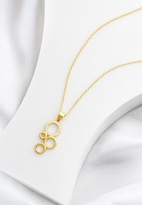 Guldkedja med tre sammanlänkade cirkulära hängen, varav ett prytt med små klara stenar, på en tunn guldkedja.