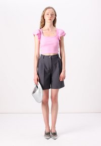 Light pink cropped top with ruffled sleeves, high-waisted dark grey shorts, silver handbag, and metallic shoes. Plain white background.