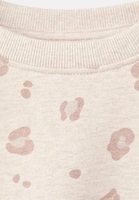 Podrobno posnetek bežnega blaga z rebrastim ovratnikom in svetlosrnkastimi abstraktnimi, nepravilnimi madeži.