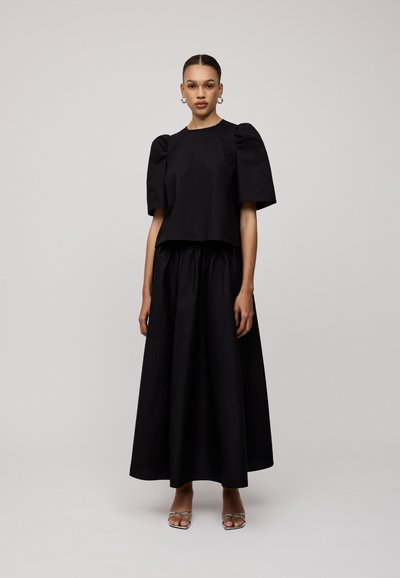 Zwart twee-delig outfit met een kort topje met pofmouwen en een lange, vloeiende rok. De stof lijkt glad en lichtgewicht te zijn.