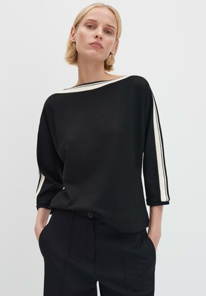 Top nero con scollatura ampia e maniche a tre quarti. Presenta strisce color crema lungo le maniche. Tessuto dalla texture liscia.