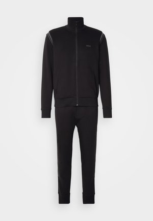 Zwart trainingspak met een ritsjack met hoge kraag, ribbelmanchetten en bijpassende tapse broek met knieaccenten. Dikke, gladde stof.