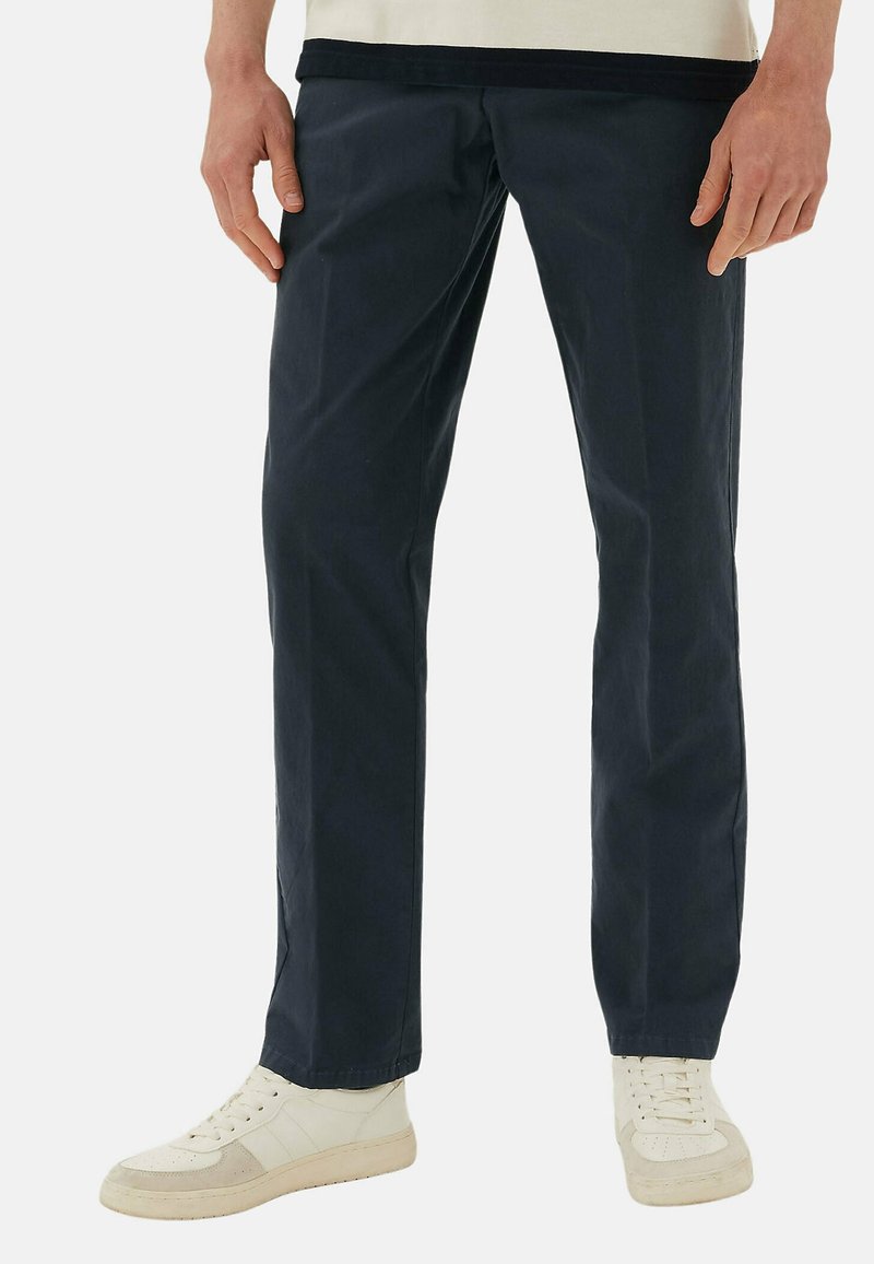 Pantalon en coton marine à coupe droite, avec une texture lisse et des poches latérales. Associé à des baskets montantes blanches.